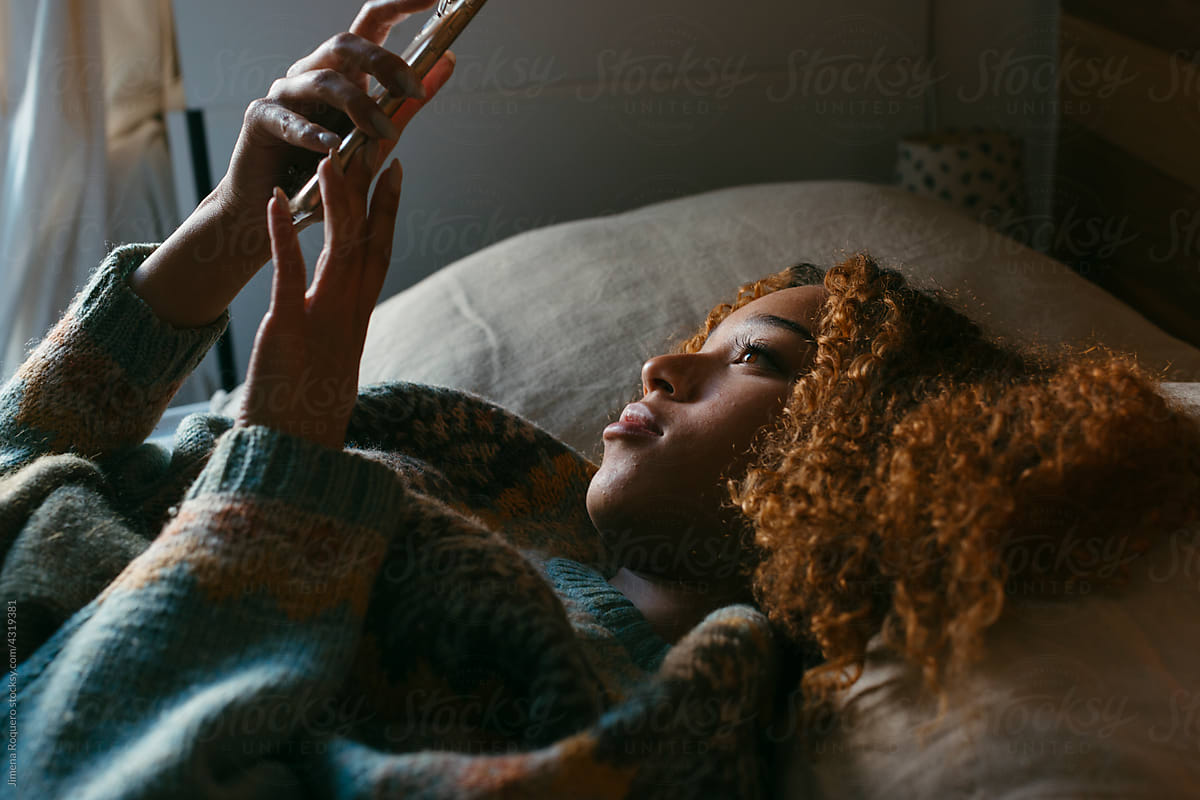 Teenage girl lying on bed checking her smartphone