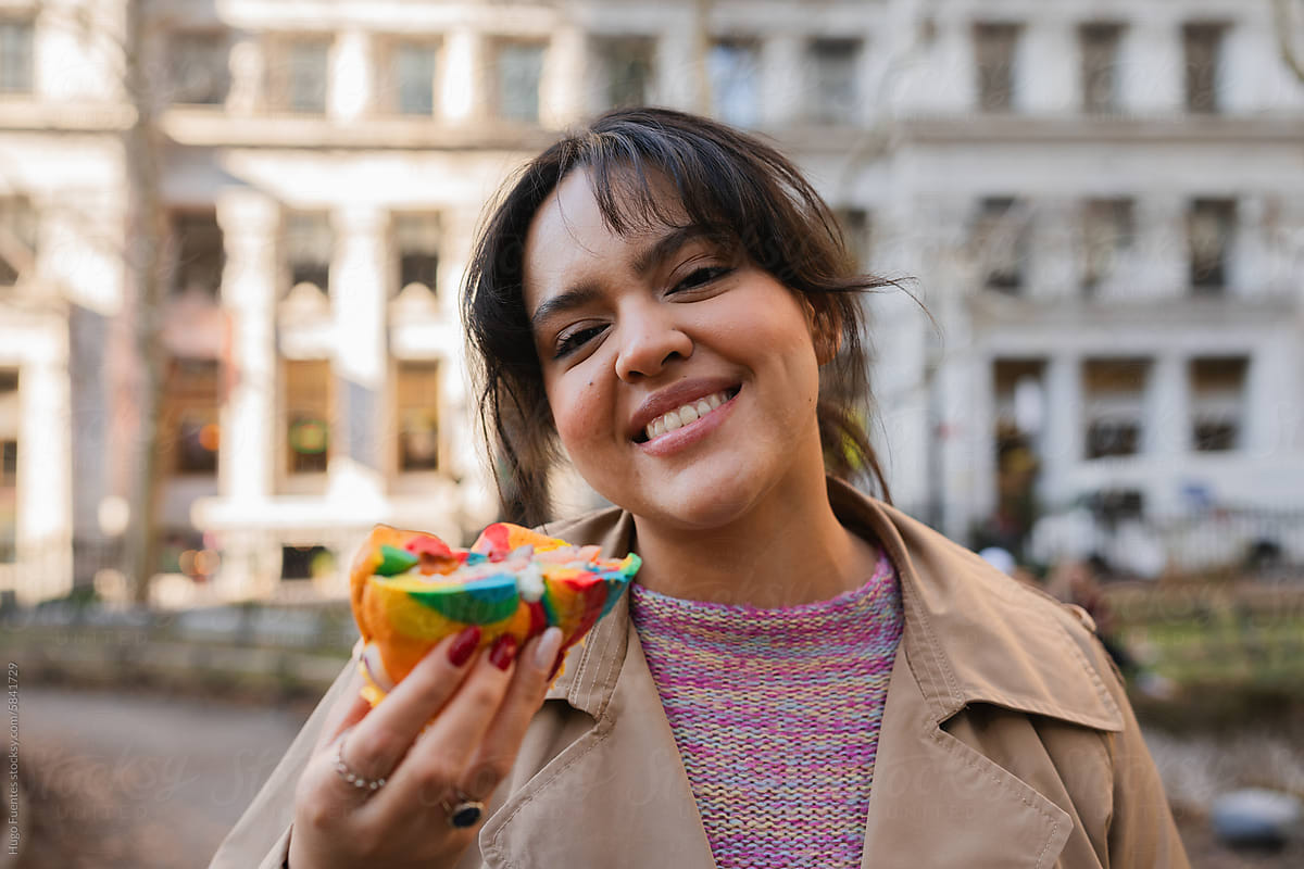 Woman smiling to the camera and holding a breakfast bagel.