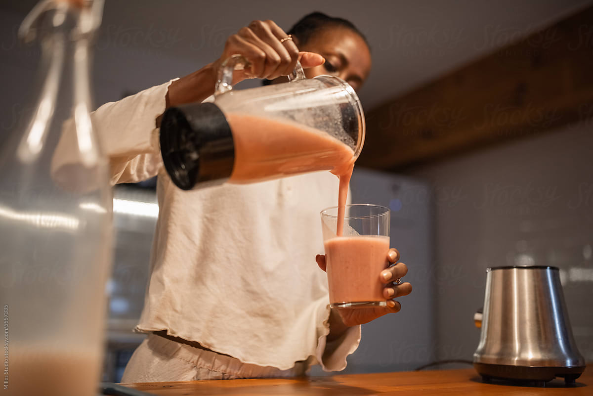 Black woman pouring smoothie from blender into glass
