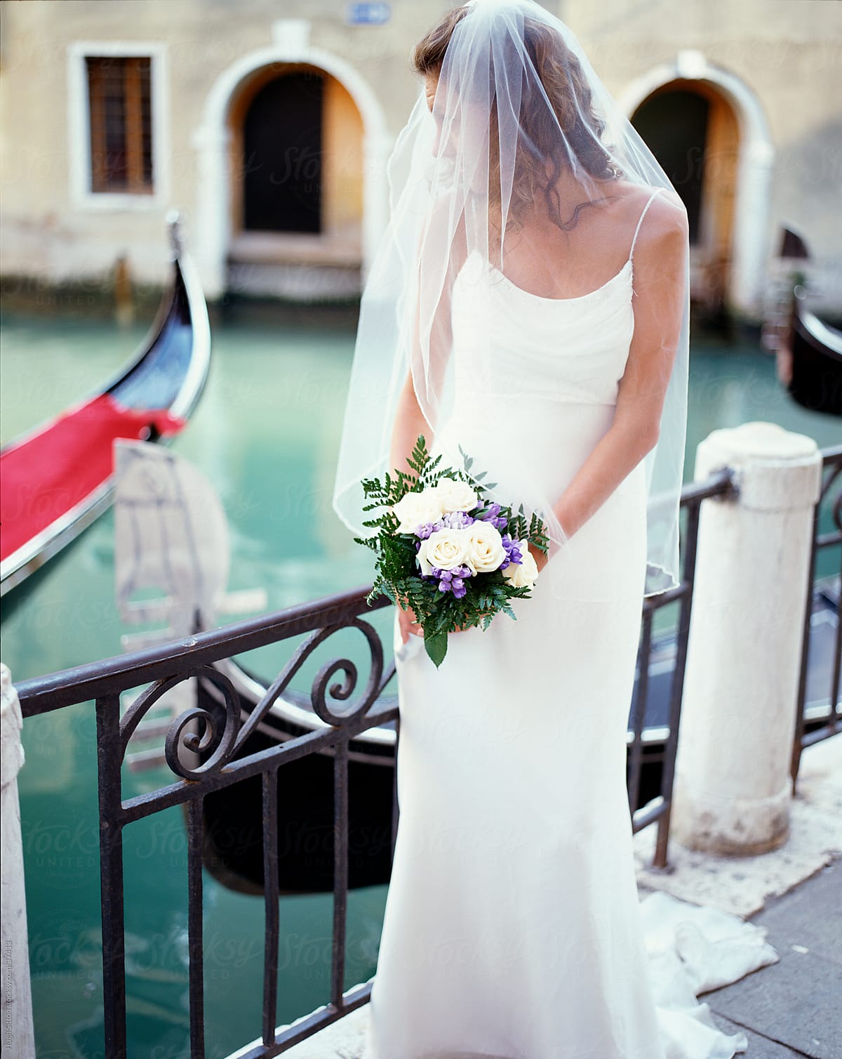Bride in wedding dress standing next to the canals of Venice.