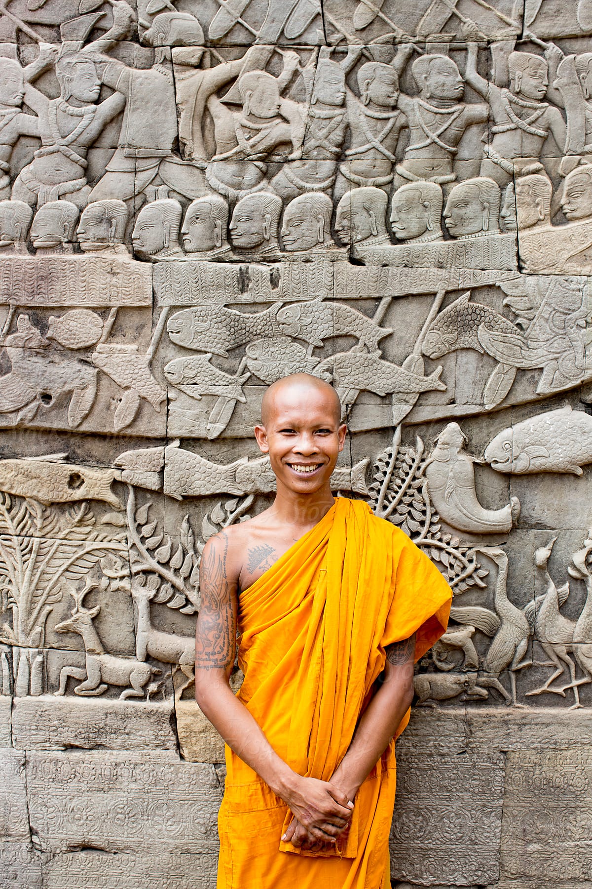 Buddhist monk standing in front of wall carvings. Bayon Temple. Angkor Wat.
