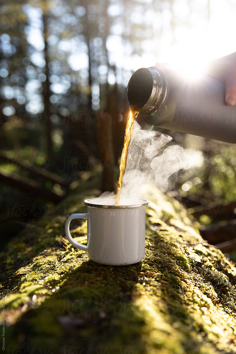 Blank white enamel mug with tea being poured into it on the forest floor