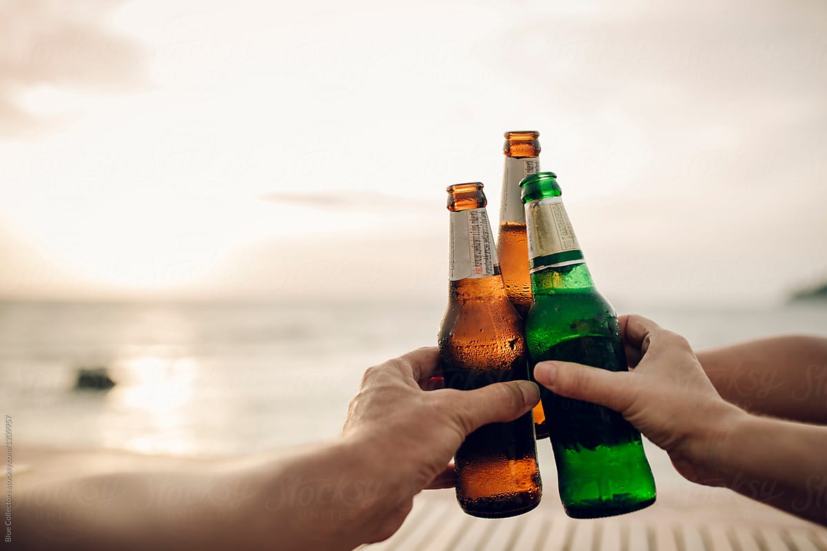 Toasting with beer bottles at sunset in the beach