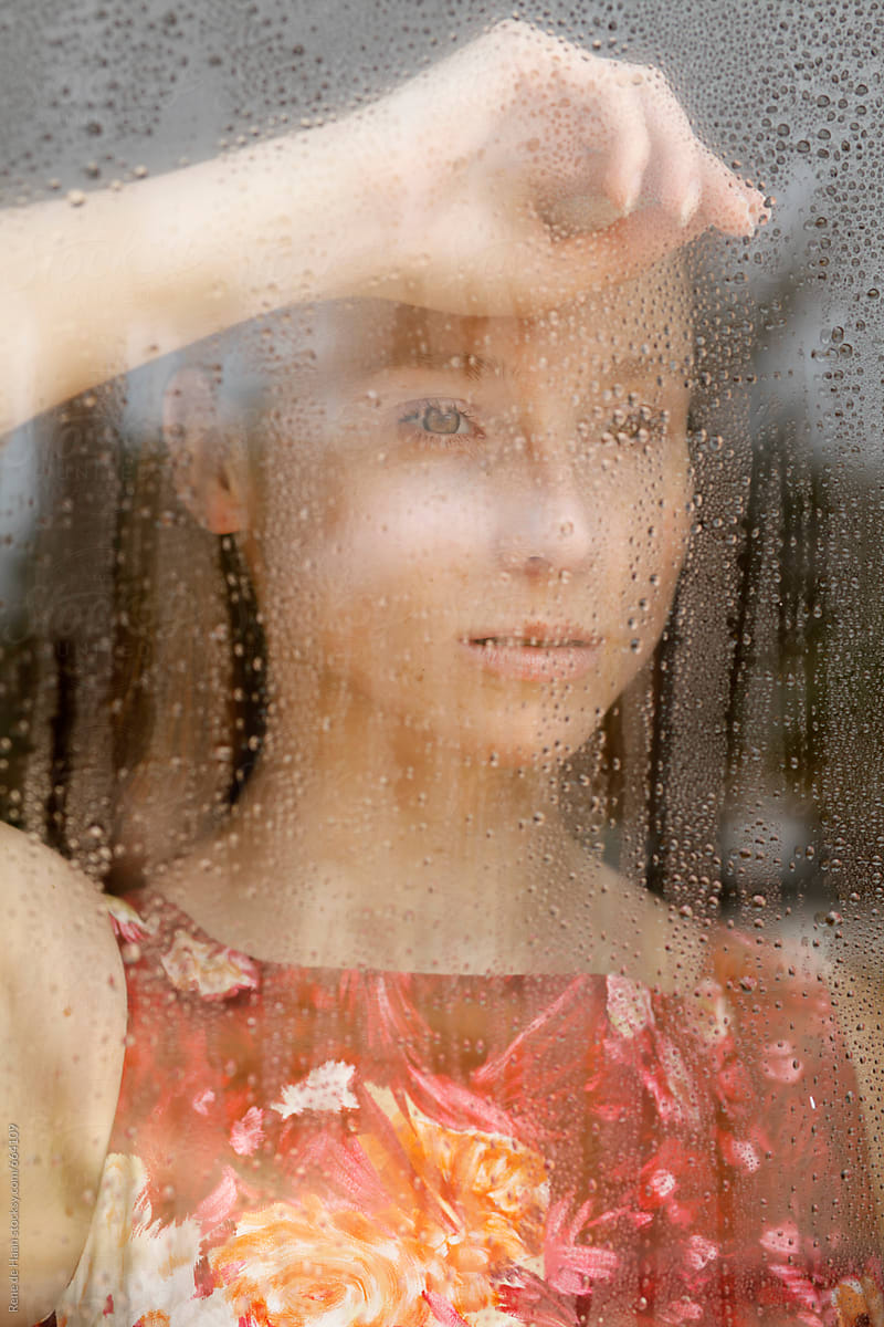 young woman looking through window with raindrops