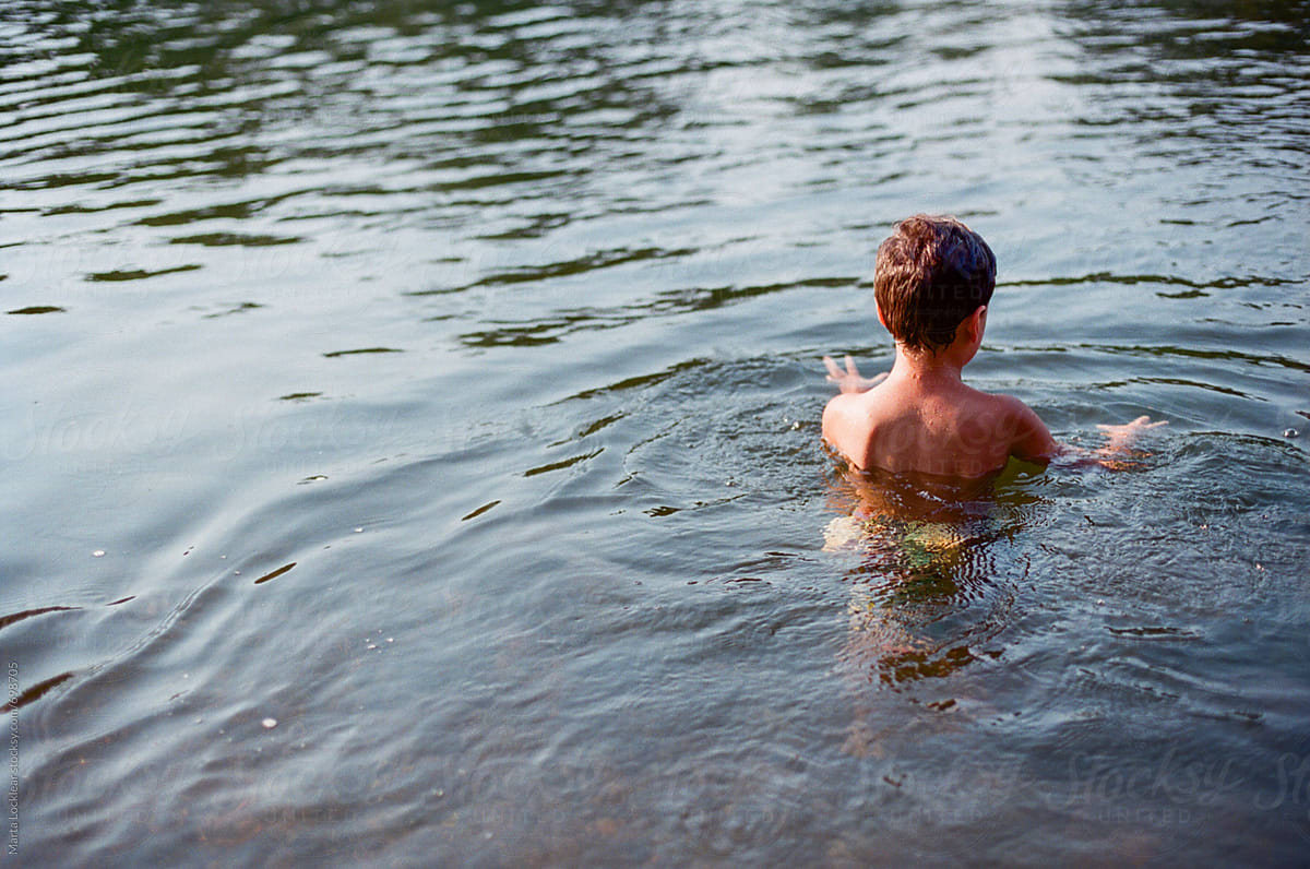 Back of a boy swimming in the river by Marta Locklear for Stocksy United.