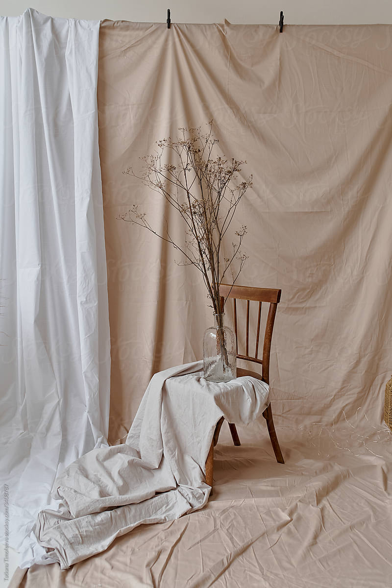 still life of dried flowers in a glass vase on a chair\
fabric with folds on the background