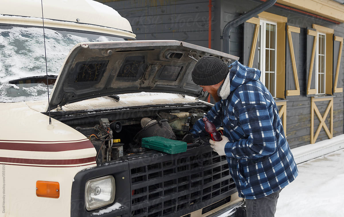 Man with bottle of coolant checking vehicle engine