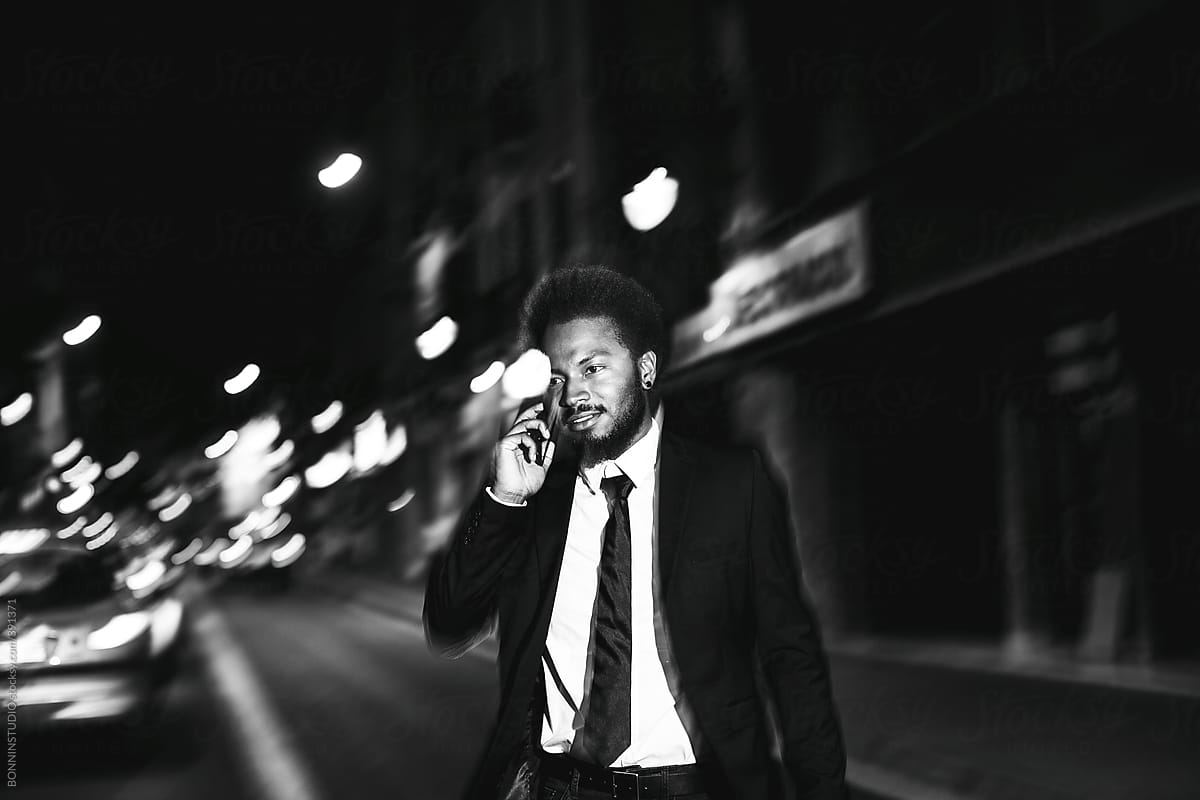 Afro businessman with mobile phone crossing the street at night.