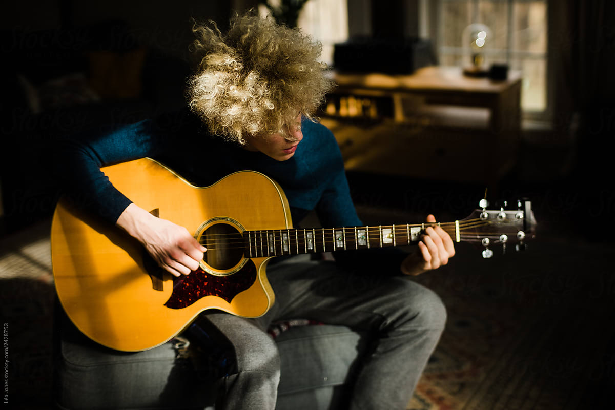 teen with blond curly hair playing guitar