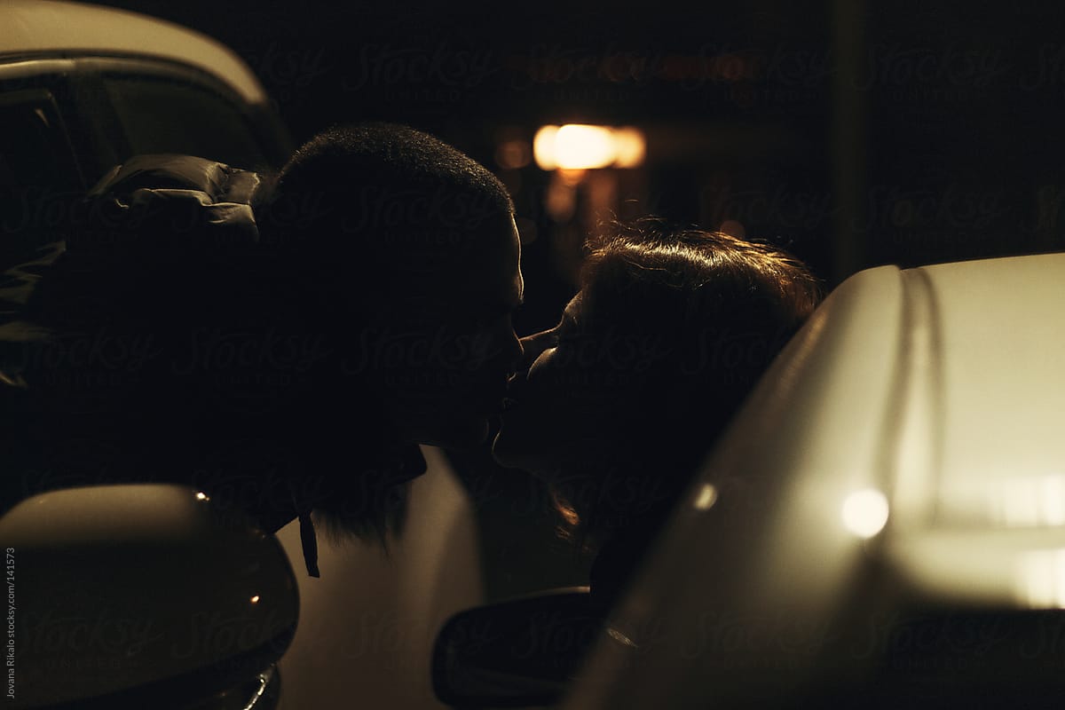 A Young Couple Leaning Out Of Their Car Windows To Kiss Each Other At Night By Jovana Rikalo