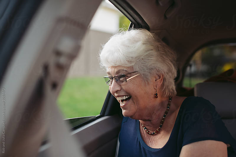 Happy, excited caucasian senior woman leaning out moving car window