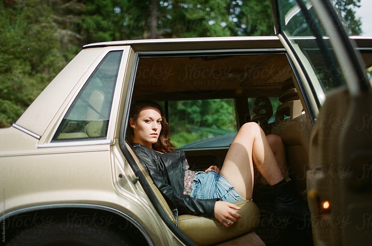 A rebellious girl sitting in the backseat of an old car