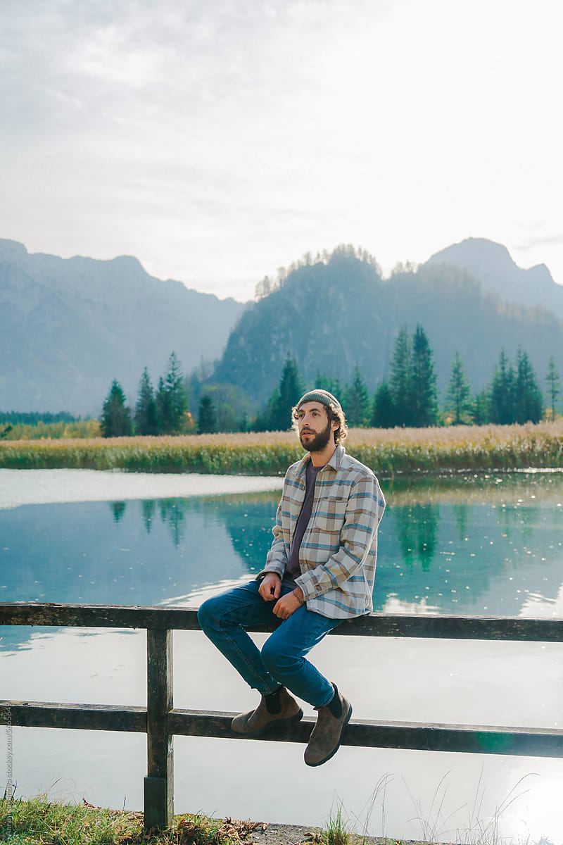Man sitting on fence on the background of alpine lake enjoying view