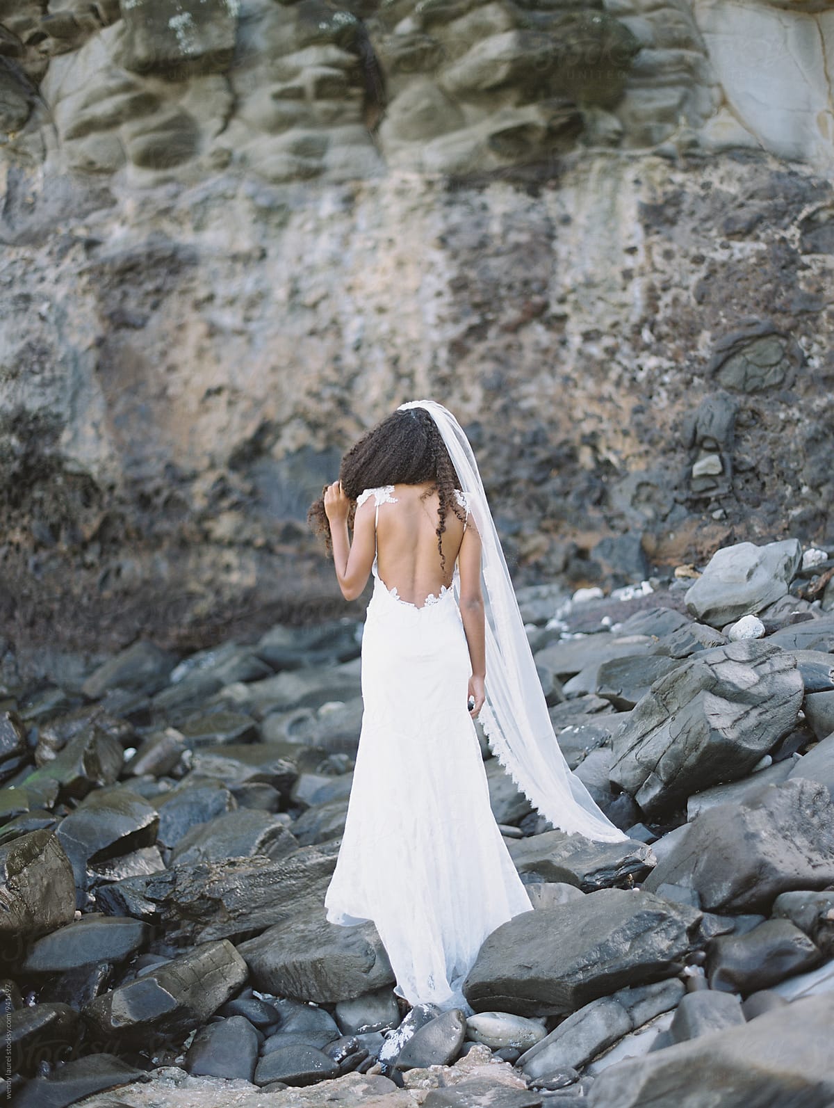 beautiful black bride on beach in gorgeous wedding gown with rocks and ocean