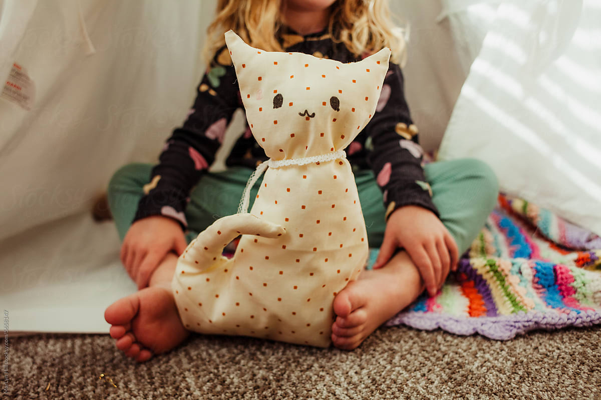 A cloth toy cat is held by child\'s feet.
