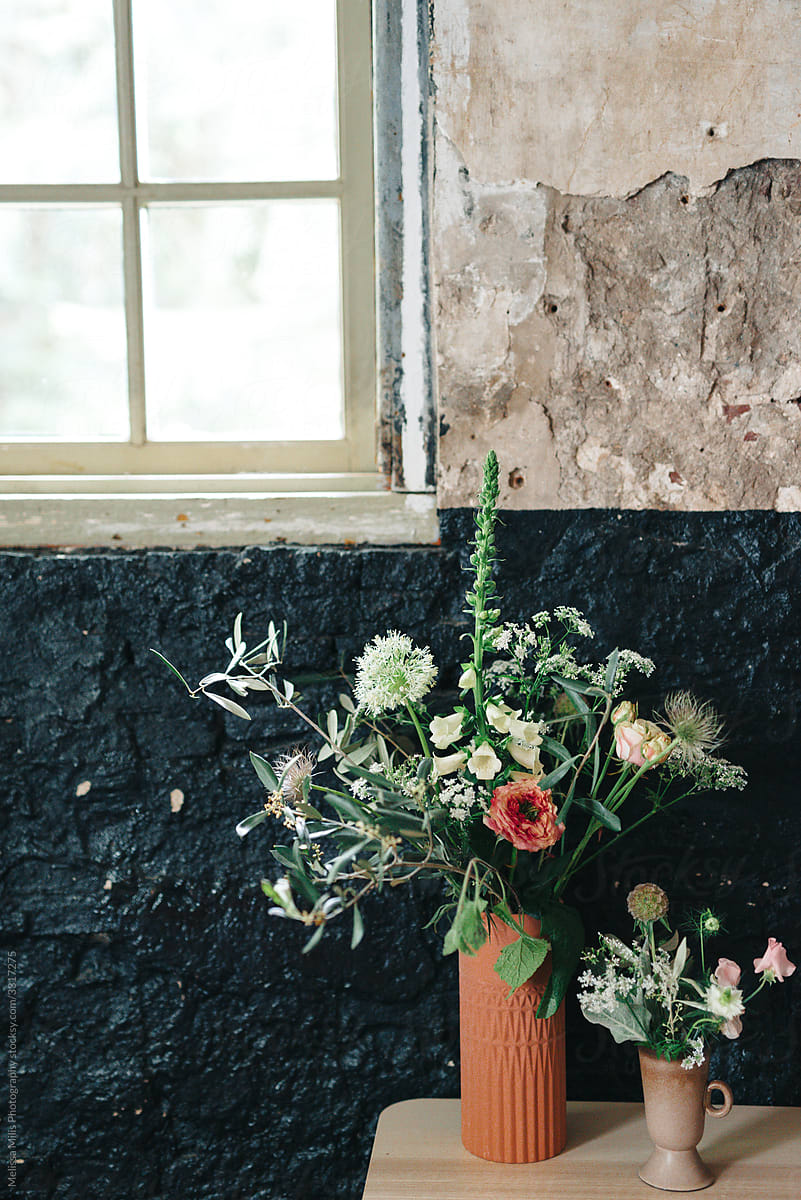 Two flower vases with cut flowers from the garden agains an industrial rustic wall