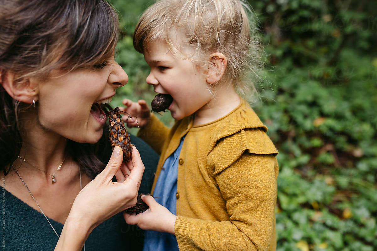 Mom and daughter goofing around with pinecones outside together.