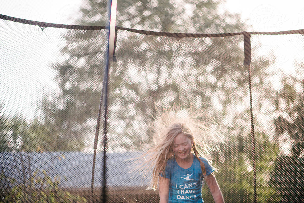 A young girl jumps on a trampoline with static in her hair.