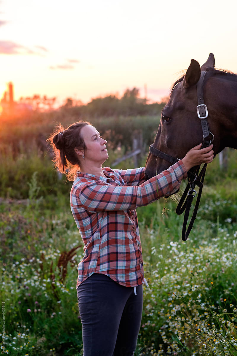 portrait of a country \
woman caring at her horse in the meadow