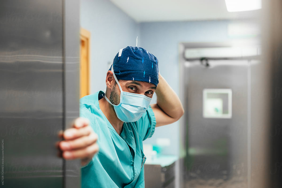 Male surgeon in uniform opening door of operating room
