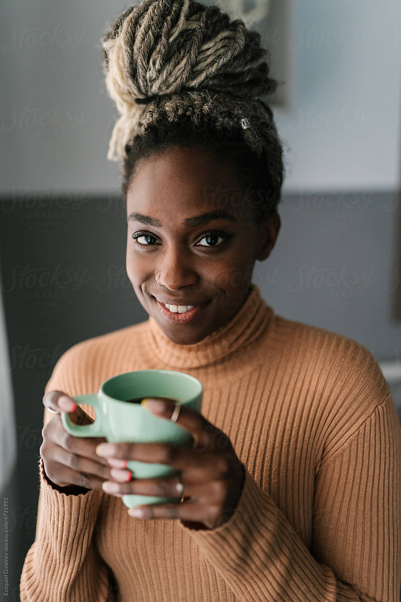 Joyful black woman with hot drink at home