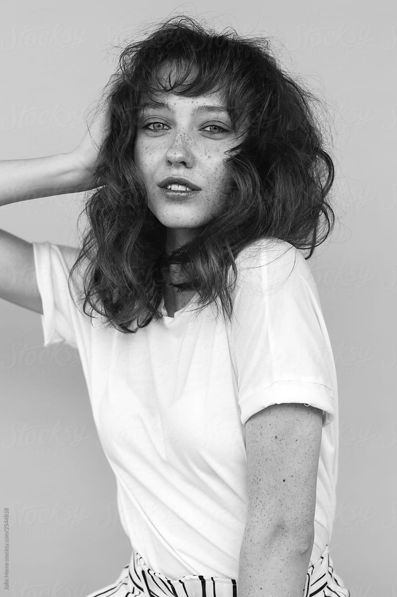 Portrait of a girl with 90th hairstyle and freckles   in white t-shirt is touching her hair