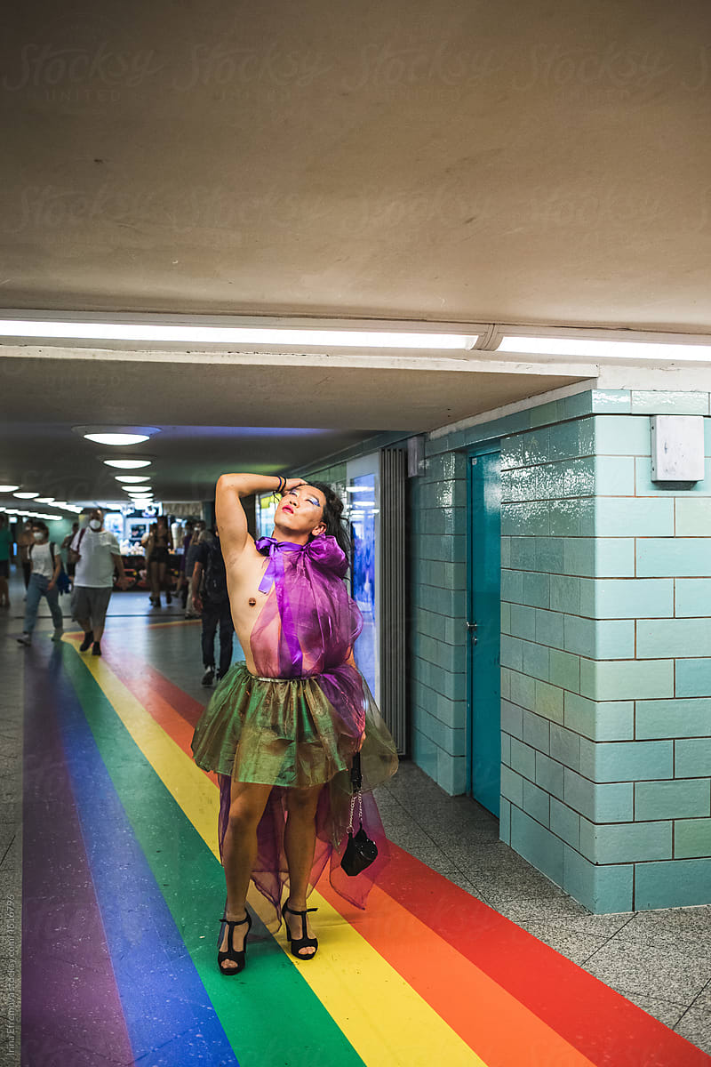 Asian man in rainbow coloured chiffon dress standing on rainbow floor