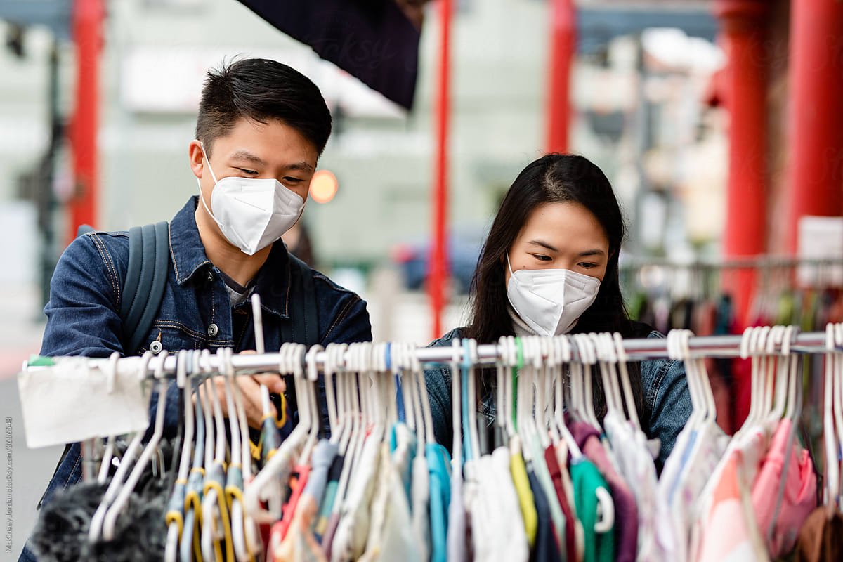 Young Asian Couple Wearing Masks Explore Clothing Rack at a Thrift Store