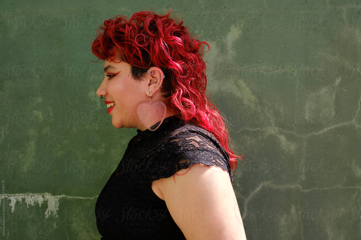 Smiling queer person with red hair over green wall in profile