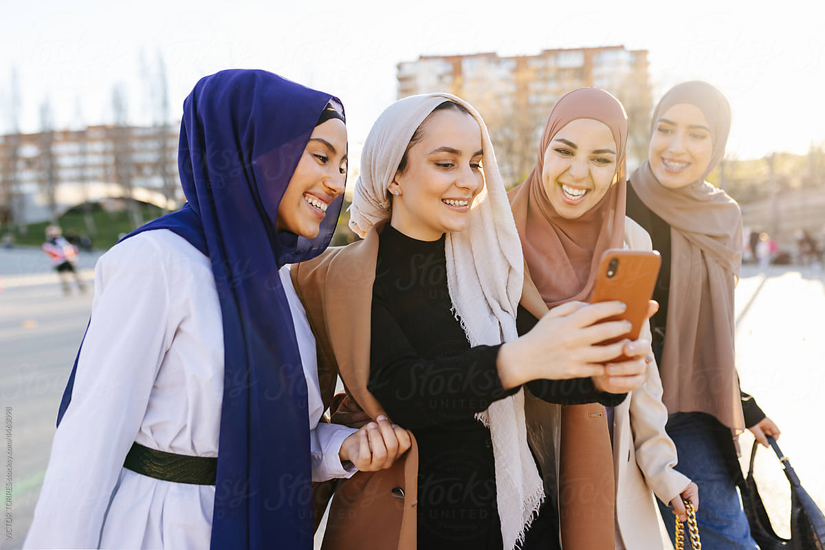 Cheerful diverse muslim women taking selfie on city street