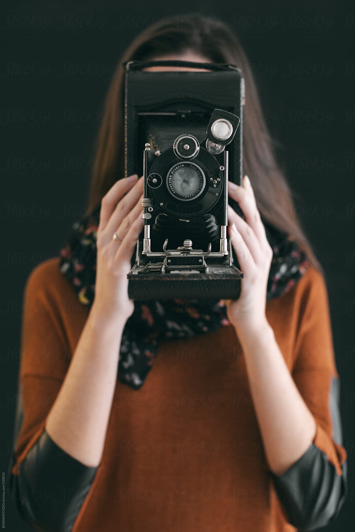 Young woman hiding her face with an old camera.