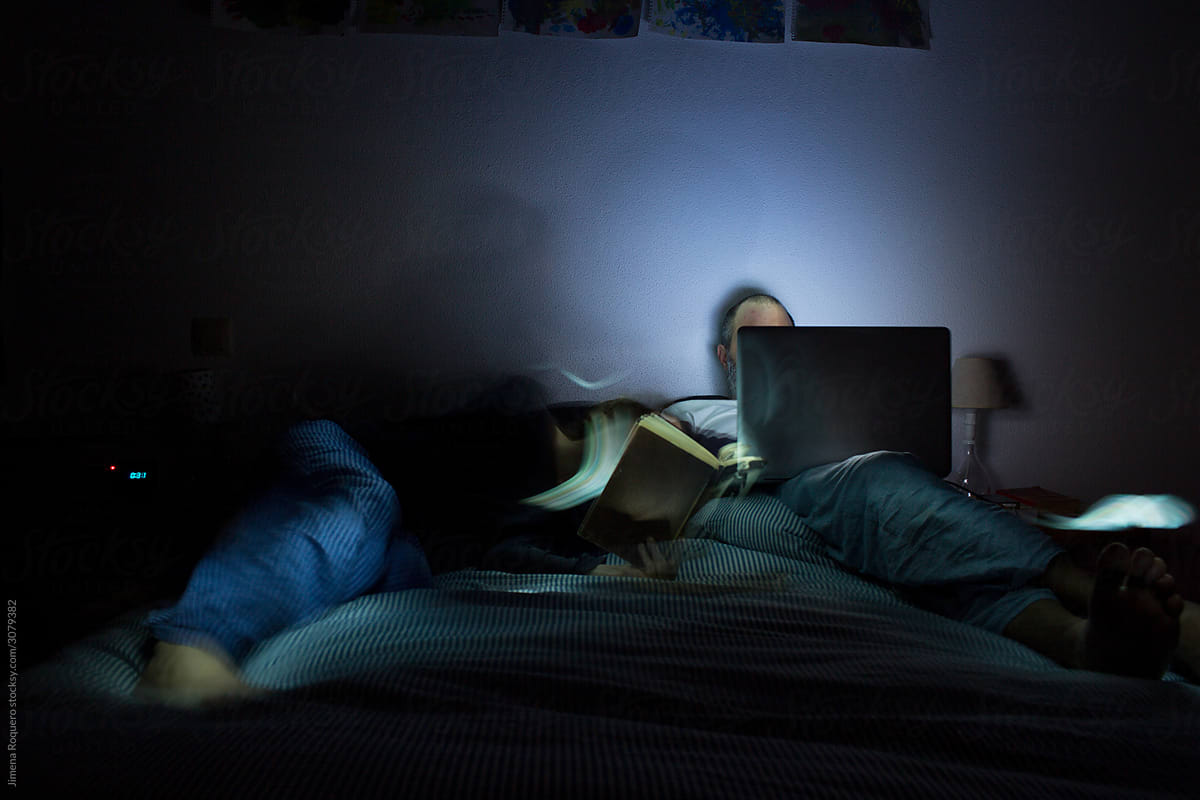 Couple lying on bed at night with laptop