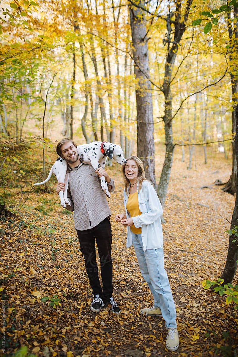 Smiling couple walking with dog in autumn forest
