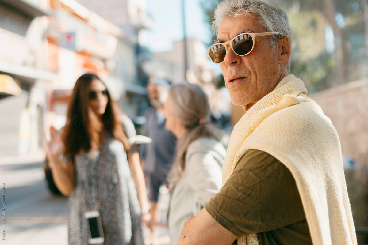 Senior man with sunglasses waiting in bus stop in sunlight in the city