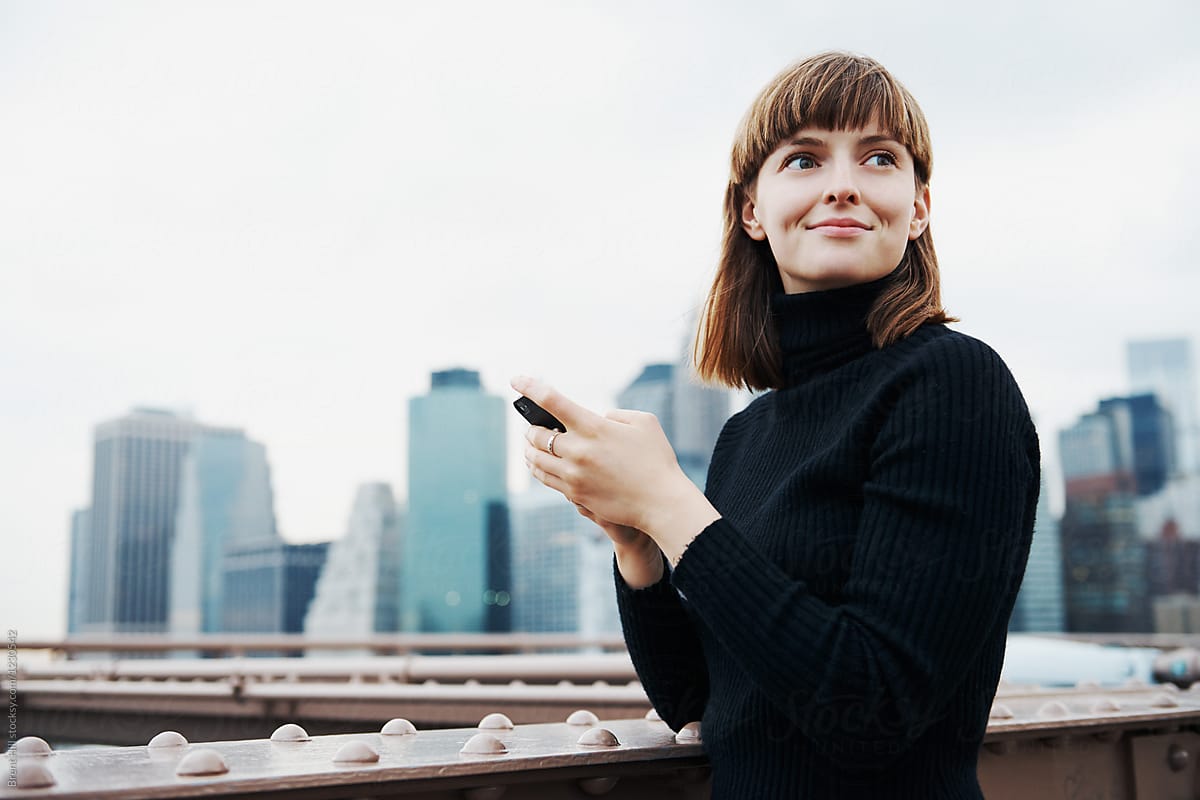 A young attractive woman texting on her smartphone with a city backdrop