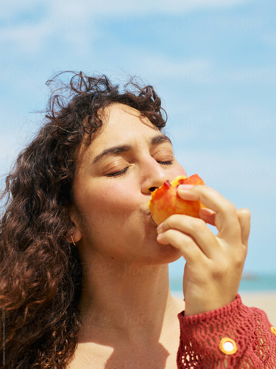 Woman biting a peach with pleasure expression at the beach