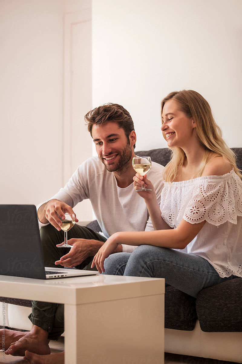 Young couple on sofa with wine and sharing laptop at home.