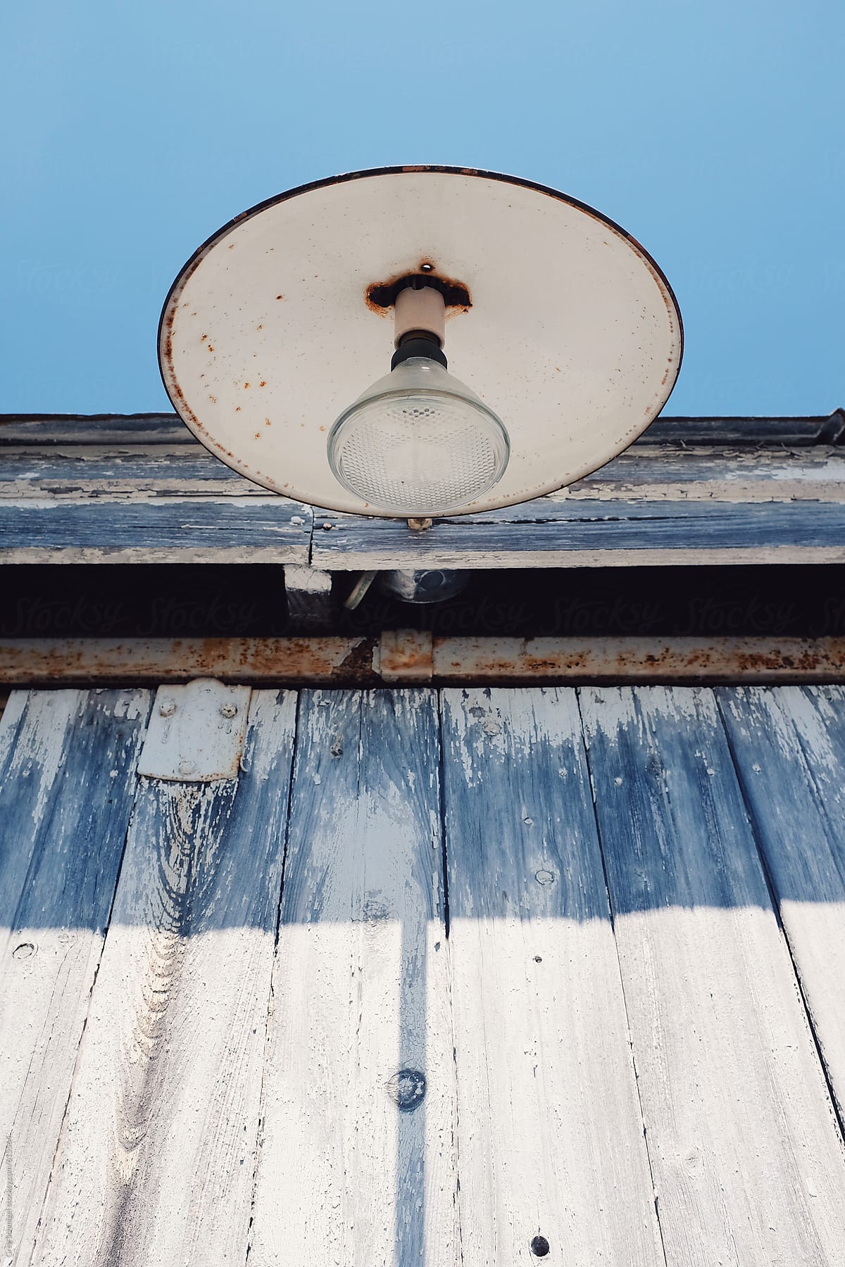 An old lamp, shade and light mounted on the side of an abandoned building