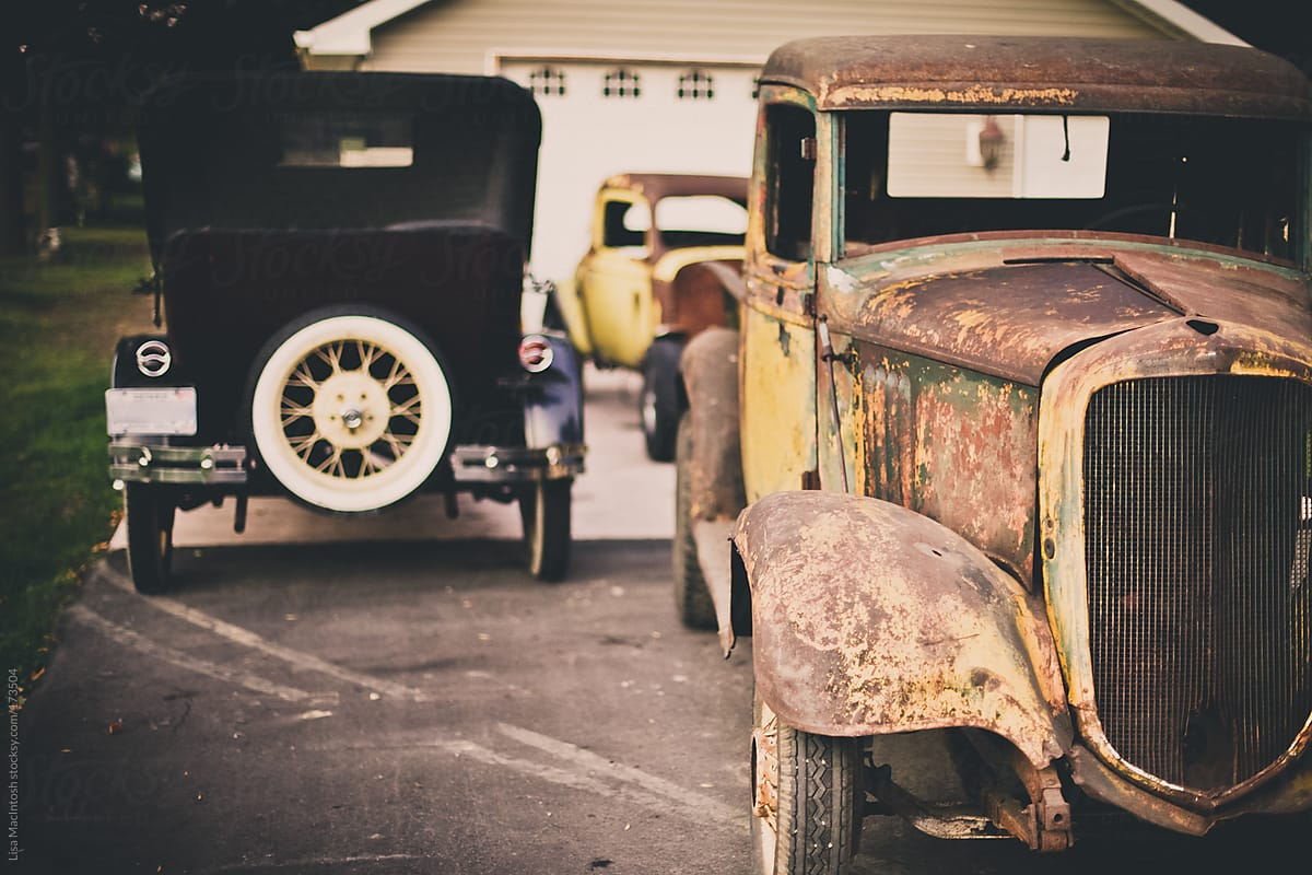three vintage, rusty automobiles in front of garage