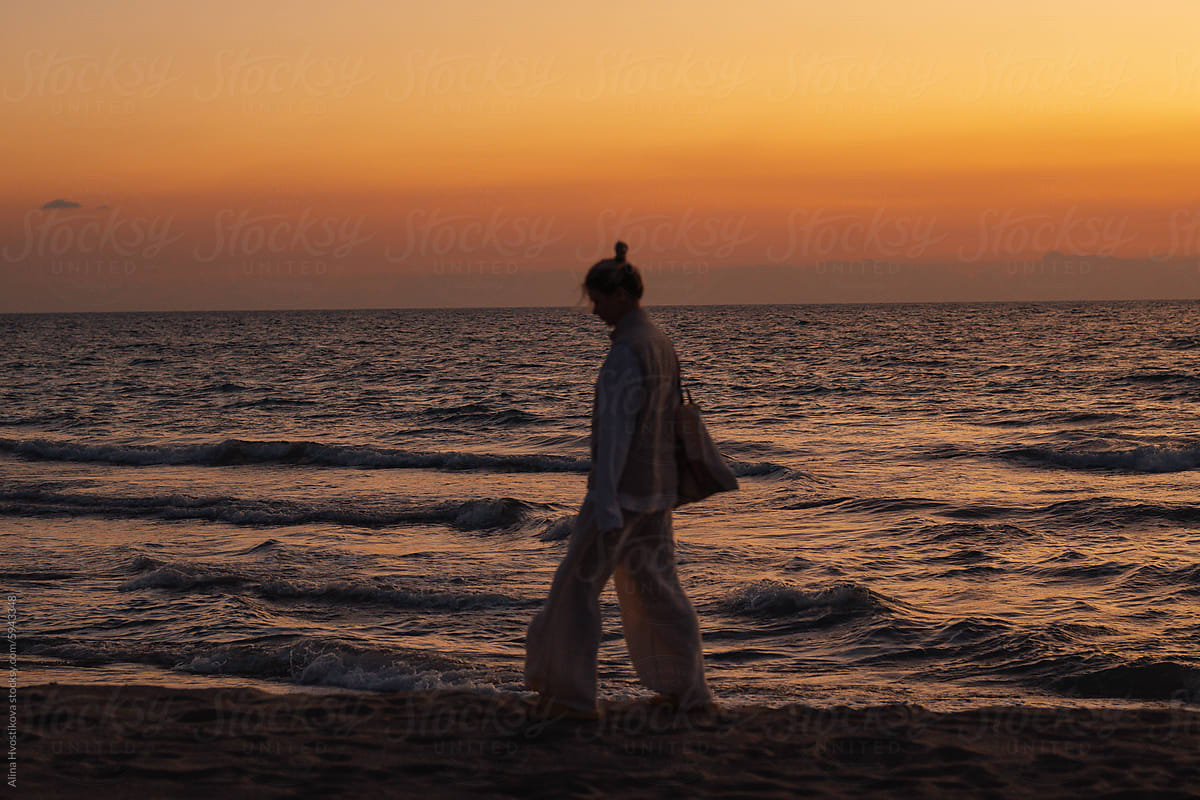 Anonymous woman walking on beach near seawater