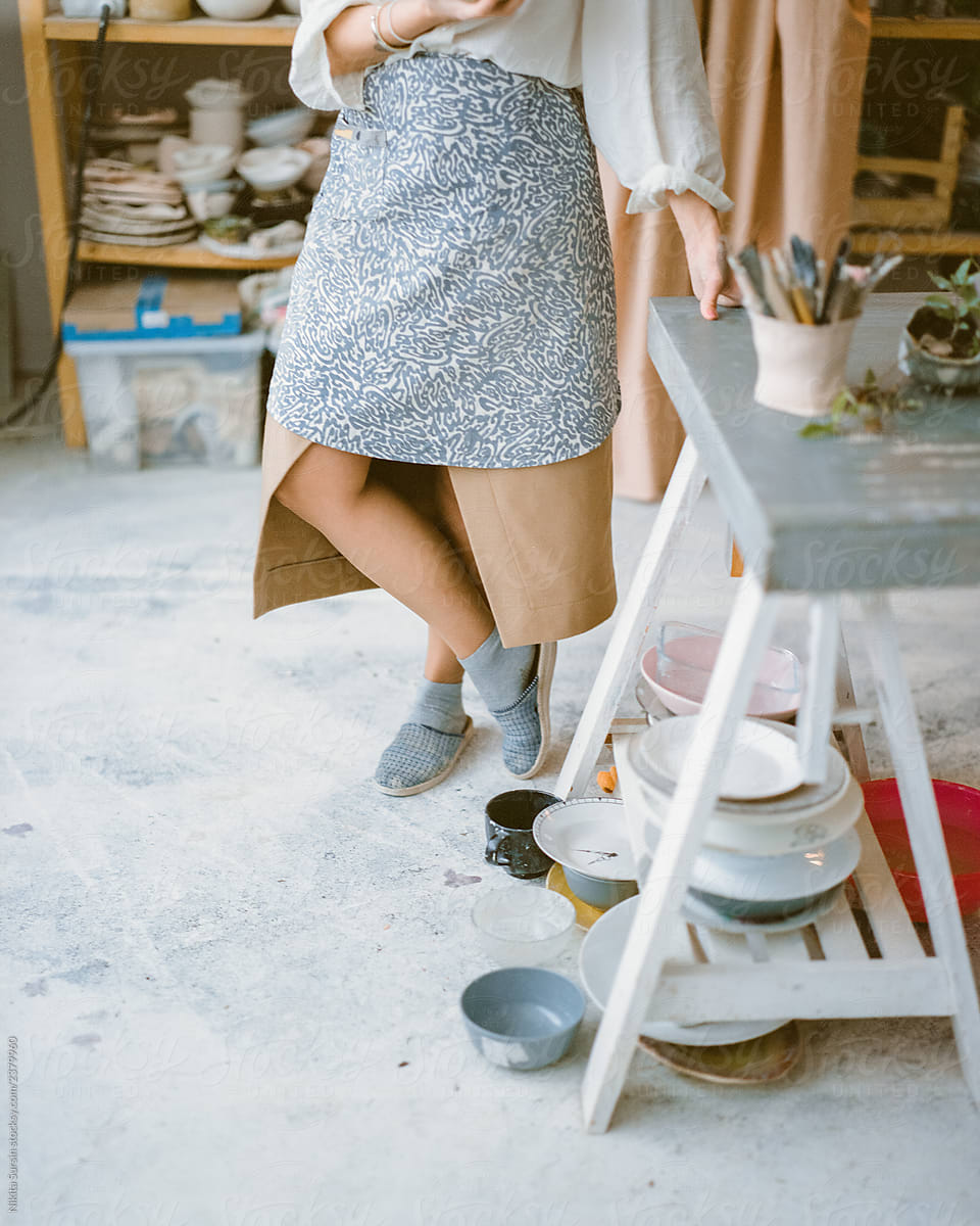girl stands cross-legged. a young artist in a skirt and apron is wearing slippers