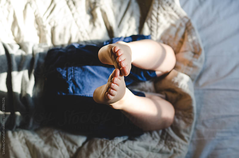 Feet and toes of child lying on bed in sunshine