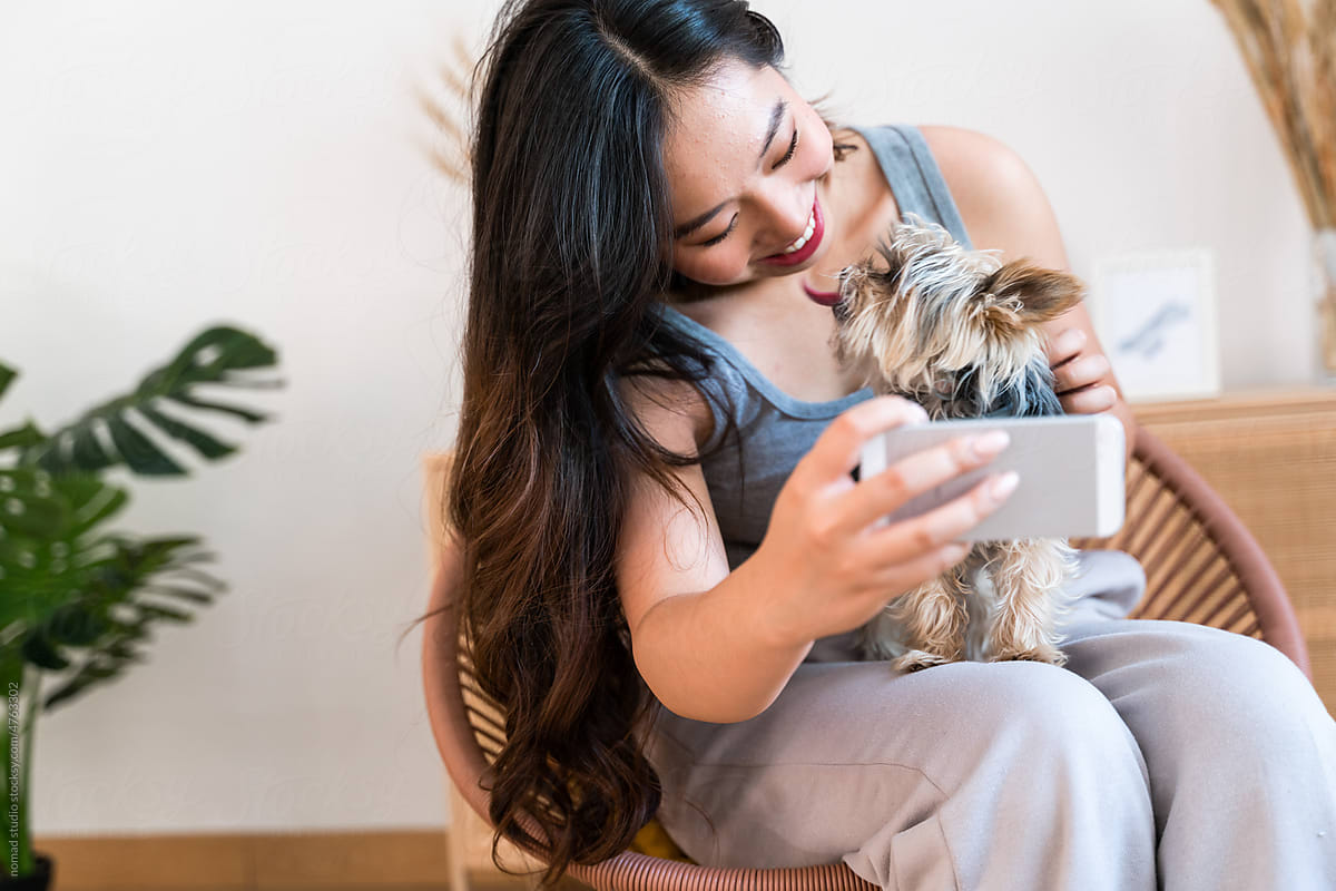 Woman taking a selfie with her little dog at home.