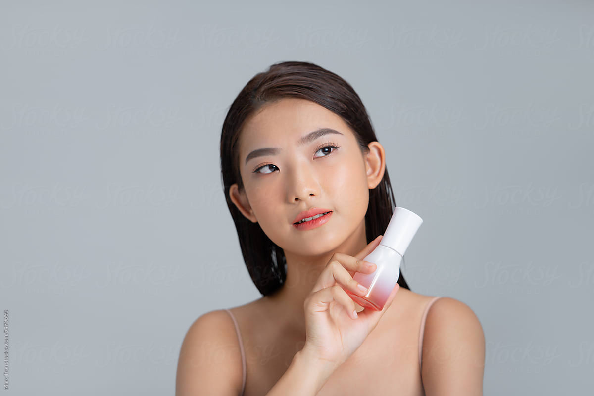 Young woman holding bottle with beauty product in studio