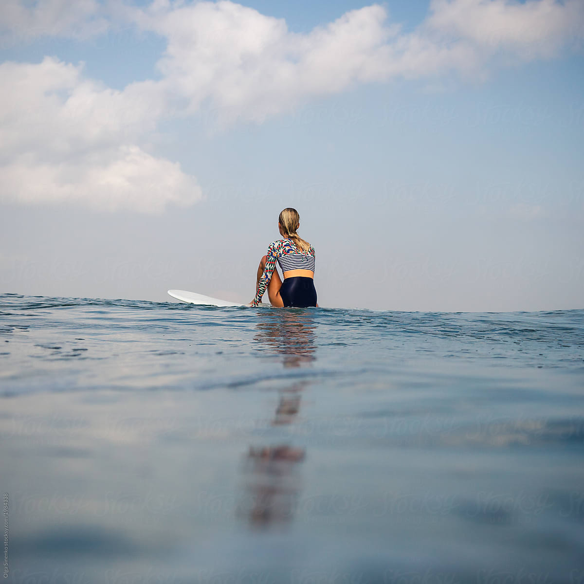 Young woman in swimsuit sitting on surf board in the ocean.