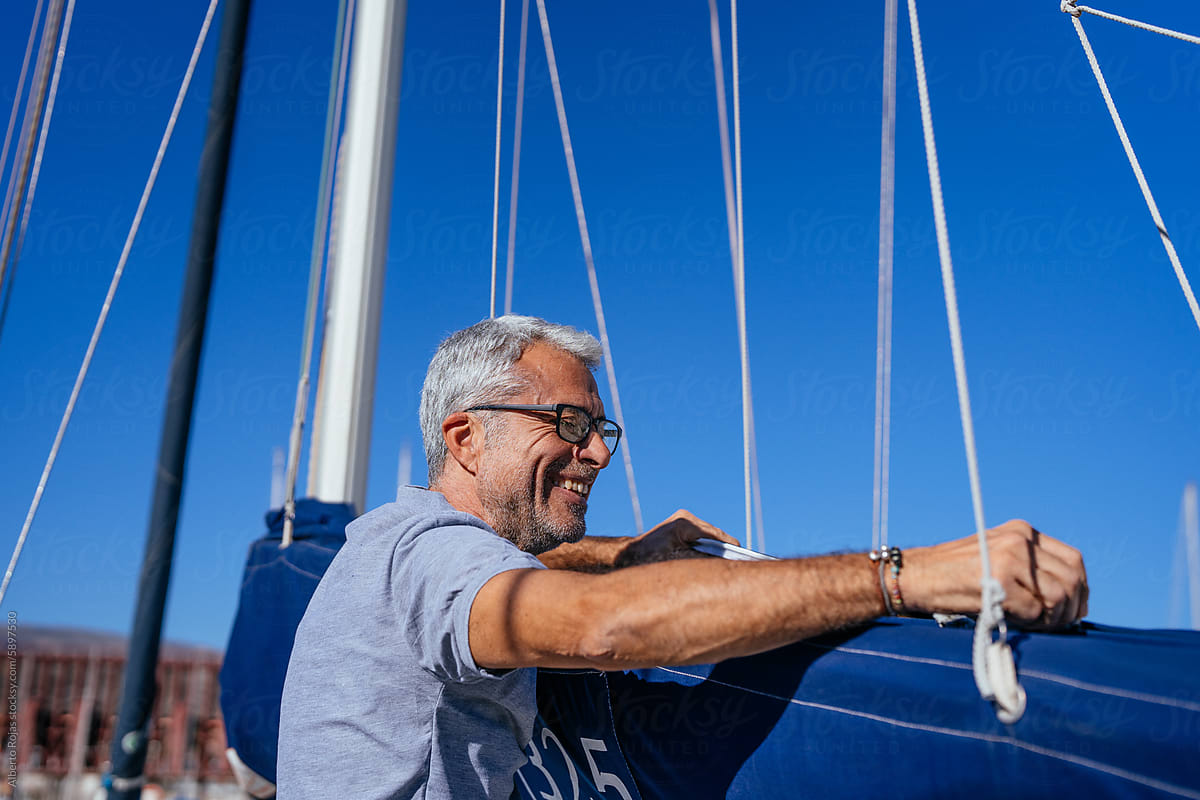 Cheerful senior man standing by yacht under blue sky