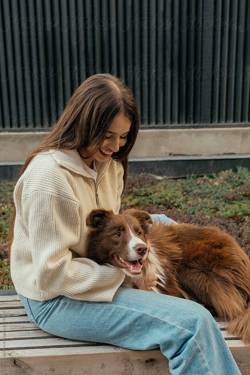 Happy woman caressing Border Collie dog while sitting on street in day