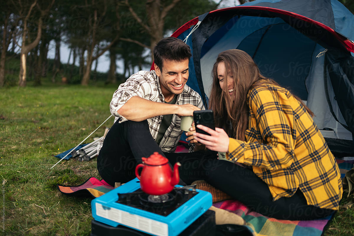 Happy couple using smartphone while camping in the forest