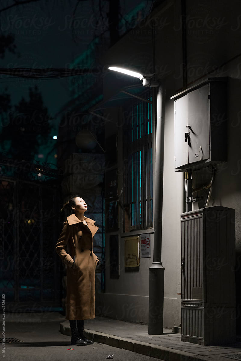 A Chinese beauty stands in the lane and transfers the street lamp