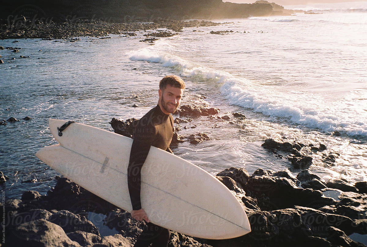 Portrait of a surfer standing on a rocky beach